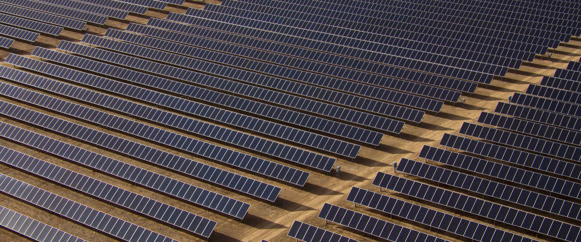 A large array of solar panels in a barren desert ground.