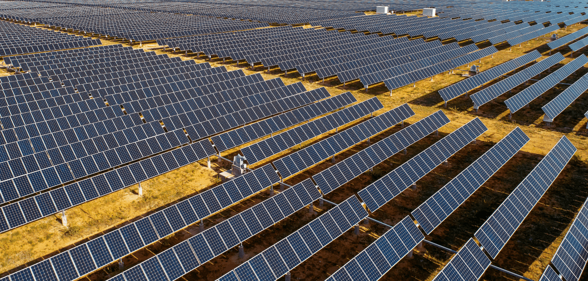 A large array of solar panels on a barren desert ground.